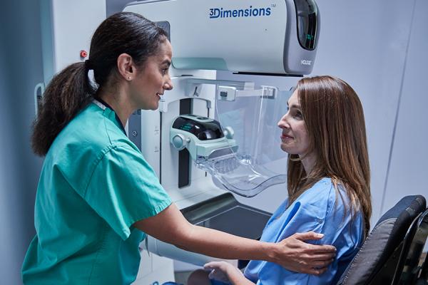 Women sitting in front of a mammography machine with a health care professional at her side.